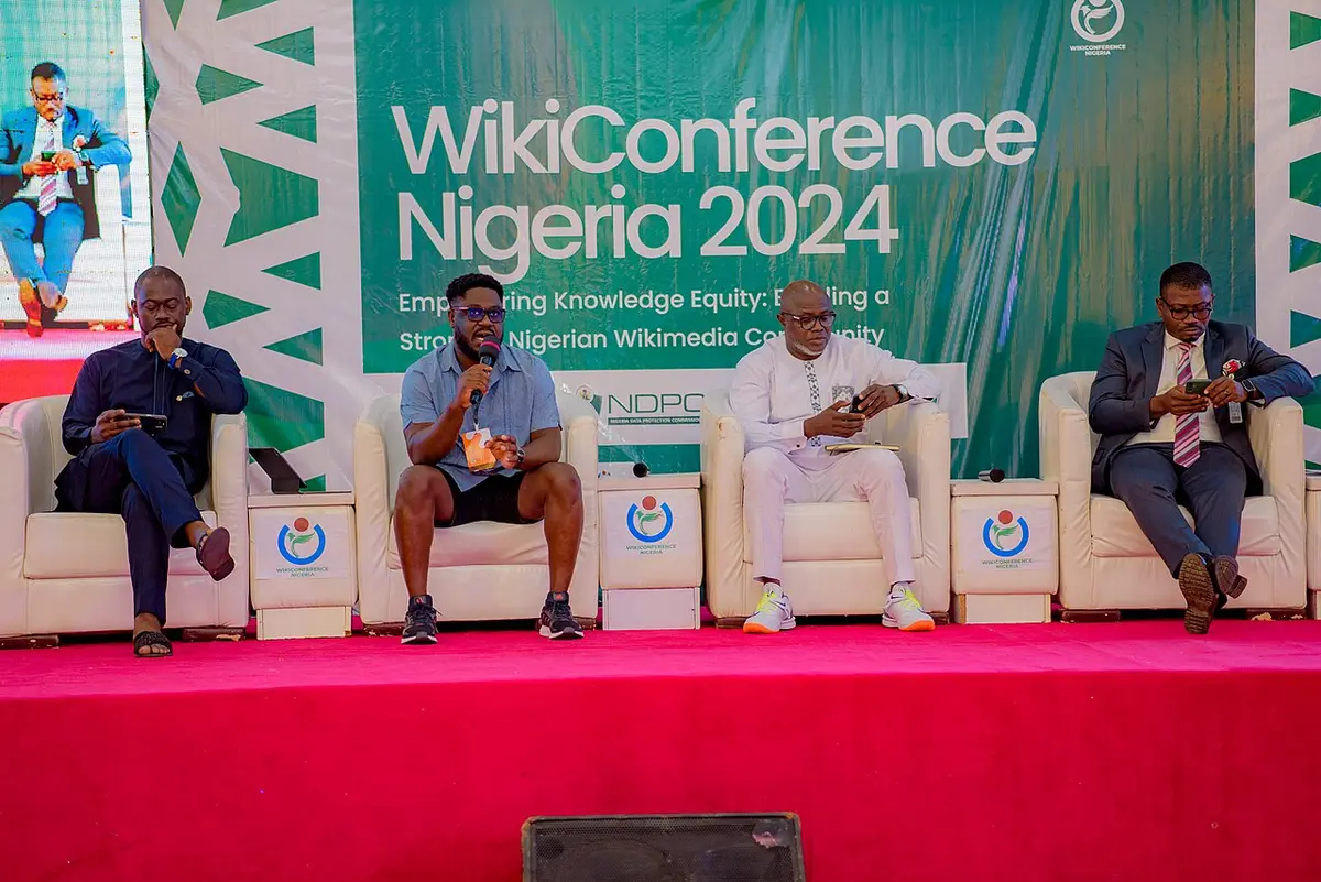 A panel of speakers seated on a conference stage in front of a branded backdrop